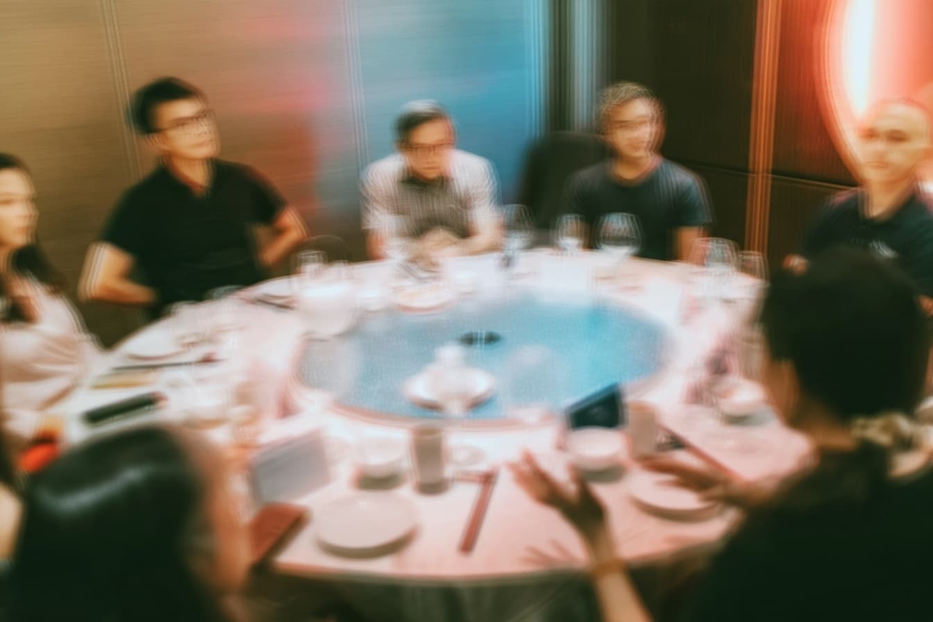 Motion-blurred view of people seated around a large round table set for a meal.